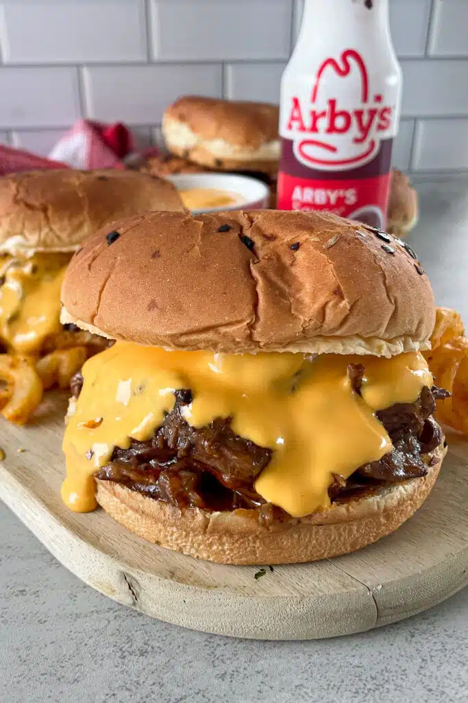 copycat Arby's beef and cheddar sandwich on a serving board with curly fries and a bottle of Arby's sauce for serving.