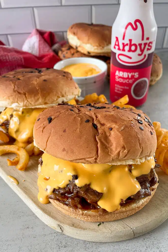 copycat Arby's beef and cheddar sandwich on a serving board with curly fries and a bottle of Arby's sauce for serving.