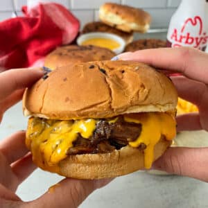close up photo of Arby's beef and cheddar held in a hand ready to be eaten.