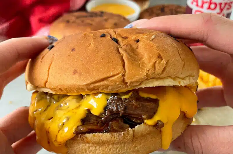 close up photo of Arby's beef and cheddar held in a hand ready to be eaten.