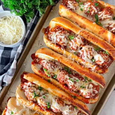 pan of 5 crock pot Italian meatballs subs ready to serve. shredded cheese and parsley in the upper left picture.