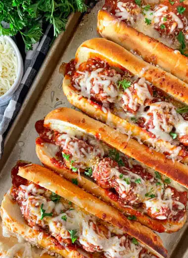 pan of 5 crock pot Italian meatballs subs ready to serve. shredded cheese and parsley in the upper left picture.