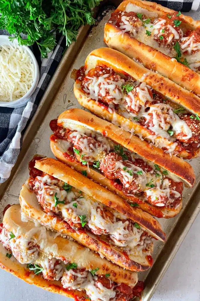 pan of 5 crock pot Italian meatballs subs ready to serve. shredded cheese and parsley in the upper left picture.