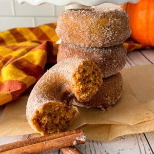 Homemade pumpkin donuts ready to serve, with photo showing one donut cut in half to show texture of donut.