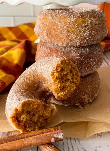 Homemade pumpkin donuts ready to serve, with photo showing one donut cut in half to show texture of donut.