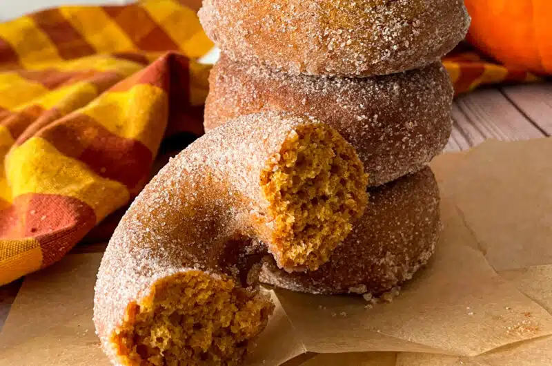 Homemade pumpkin donuts ready to serve, with photo showing one donut cut in half to show texture of donut.