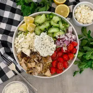 Healthy Greek Chicken bowl with tzatziki ready to serve with a side of feta cheese and lemons