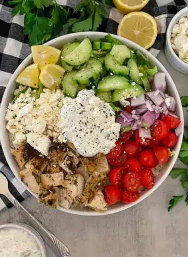 Healthy Greek Chicken bowl with tzatziki ready to serve with a side of feta cheese and lemons