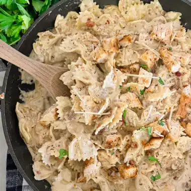 Skillet chicken bacon ranch pasta ready to serve with a side of bacon crumbles, parmesan cheese, and fresh basil.