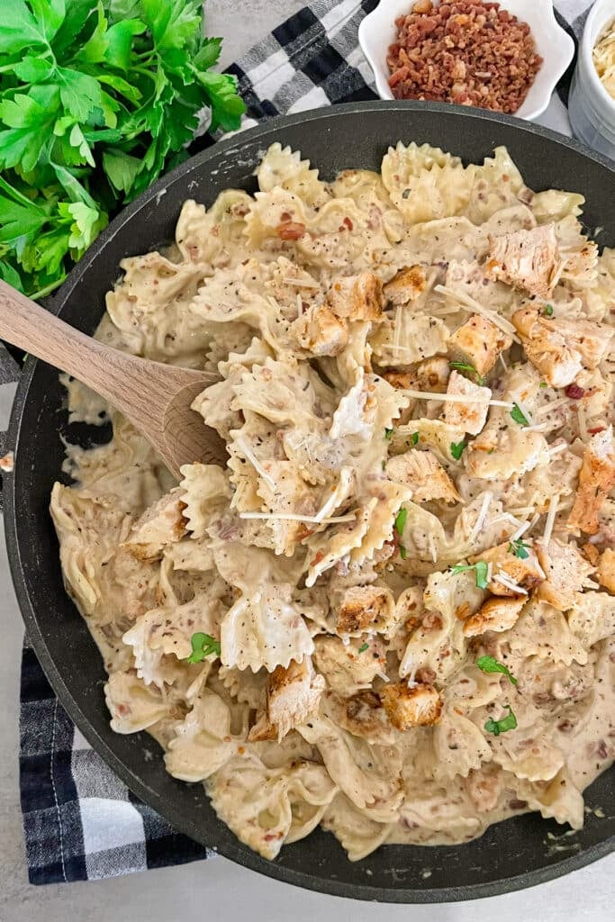 Skillet chicken bacon ranch pasta ready to serve with a side of bacon crumbles, parmesan cheese, and fresh basil.