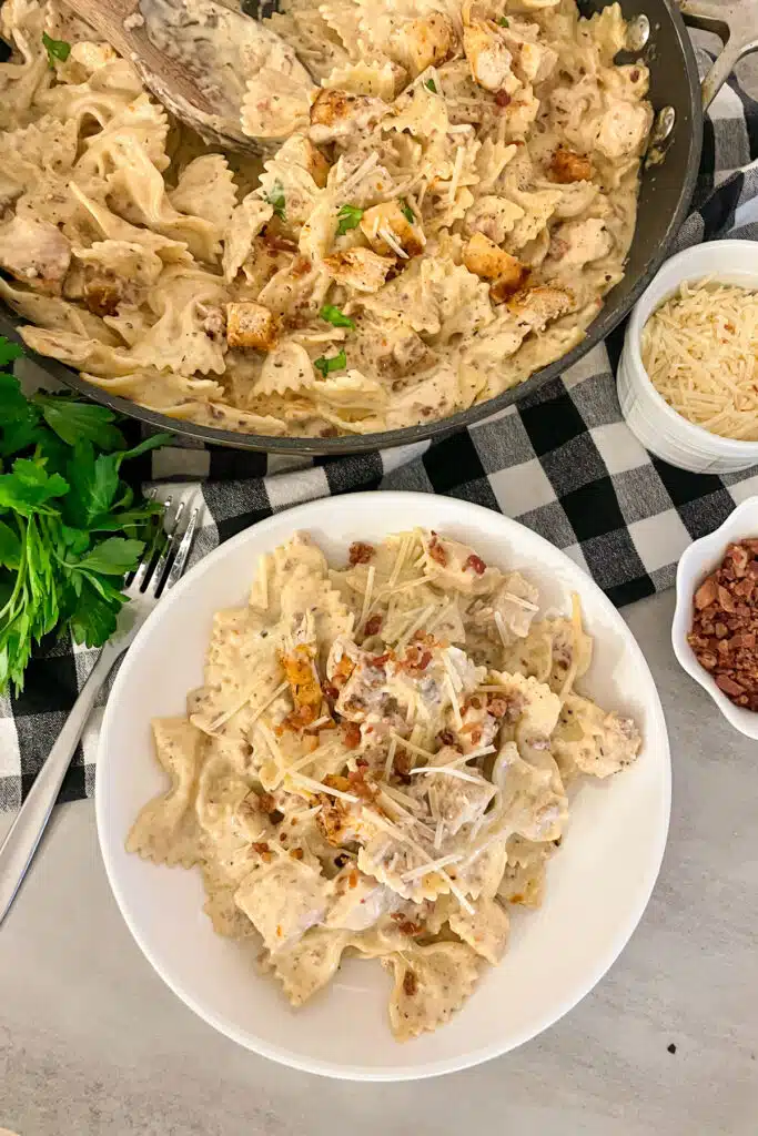 Bacon ranch chicken pasta served on a white serving plate topped with bacon crumbles and shredded cheese.