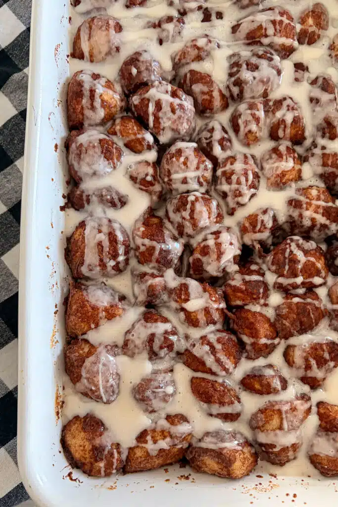 baked cinnamon roll bites shown in baking dish drizzled with frosting before serving.