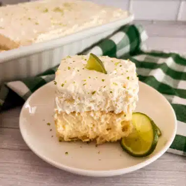 Slice of no-bake key lime pie lush on a white serving plate with limes on the side