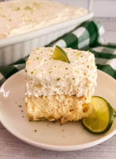 Slice of no-bake key lime pie lush on a white serving plate with limes on the side