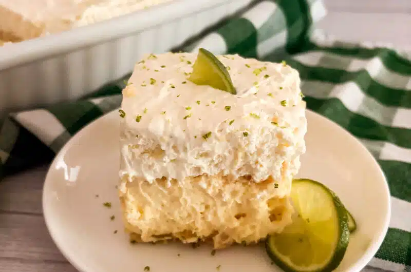 Slice of no-bake key lime pie lush on a white serving plate with limes on the side