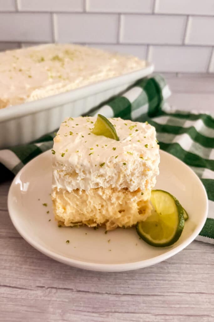 Slice of no-bake key lime pie lush on a white serving plate with limes on the side