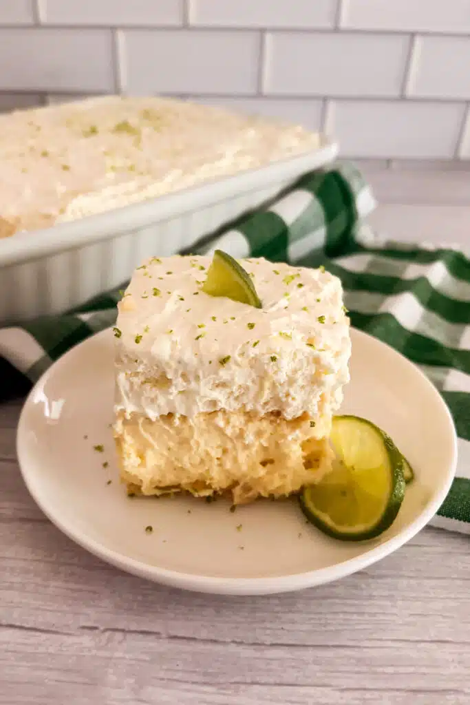 Slice of no-bake key lime pie lush on a white serving plate with limes on the side