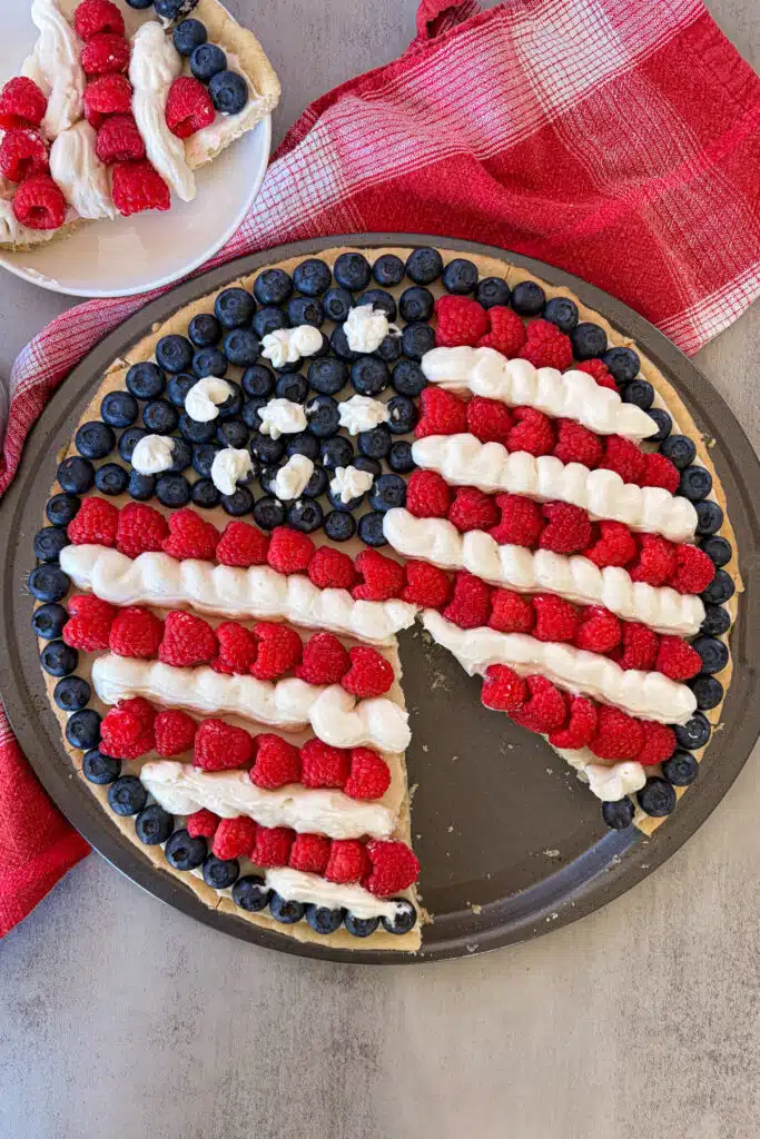 patriotic fruit pizza with a slice cut out and placed on a plate for serving. 